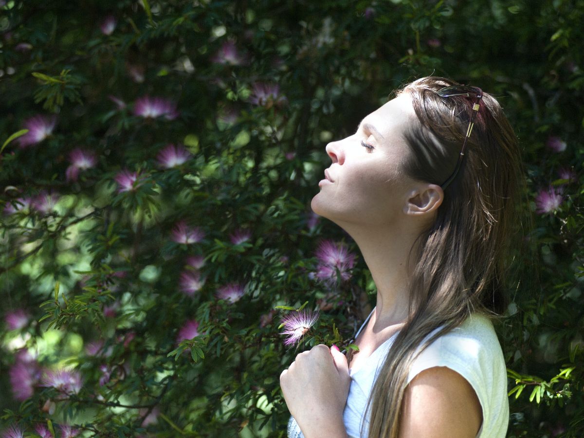 Woman closing her eyes standing against sunlight near flower garden