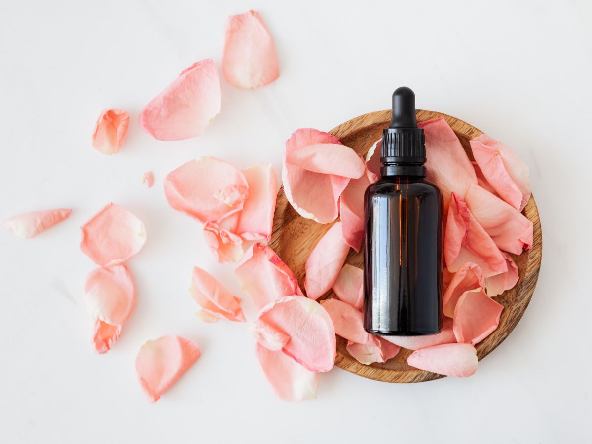 A cosmetic oil with pink rose petals and wooden plate